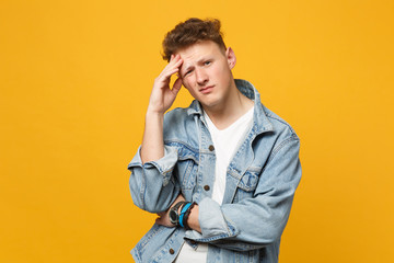 Portrait of puzzled young man in denim casual clothes looking camera, putting hand on head isolated on yellow orange wall background. People sincere emotions, lifestyle concept. Mock up copy space.