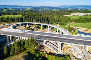 Fototapeta premium New highway under construction in Poland on national road no 7, E77, called Zakopianka. Overpass crossroad with viaducts and arc near Naprawa village. Aerial view in June 2019