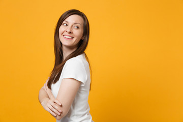 Obraz premium Side view of smiling young woman in white casual clothes holding hands crossed, looking aside isolated on bright yellow orange wall background in studio. People lifestyle concept. Mock up copy space.