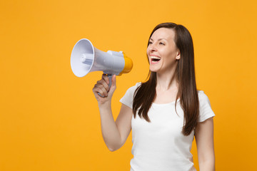 Portrait of laughing young woman in white casual clothes looking aside, scream in megaphone isolated on bright yellow orange wall background in studio. People lifestyle concept. Mock up copy space.