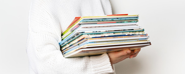 Girl in a white woolen sweater holding a stack of children's books on white background with copy space. Long wide banner