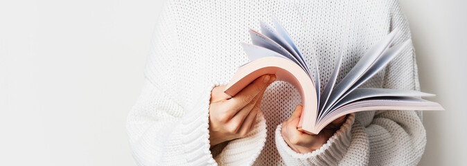 Close view of woman in white woolen sweater holding an open book with pink cover in hands. Long...