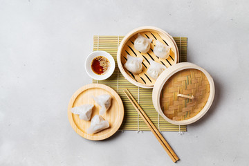 Traditional chinese steamed dumplings Dim Sums in bamboo steamer with sauce and chopsticks on light surface with copy space. Flat lay composition Asian food background.