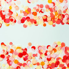 Colorful frame made with red and orange festive confetti on pastel background.