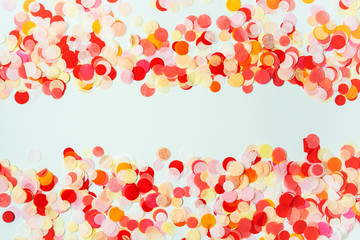 Colorful frame made with red and orange festive confetti on pastel background.