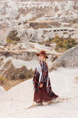 Beautiful traveling woman wearing authentic boho chic style poncho and hat have a fun in Cappadocia valley, Turkey. Travel and wanderlust concept. Copy space background.