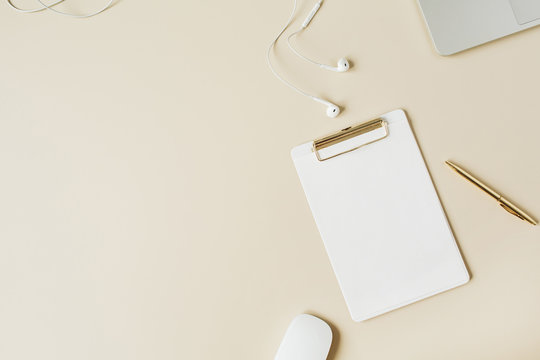 Minimalist home office desk workspace with clipboard, laptop, headphones on beige background. Flat lay, top view modern lifestyle copy space blank mockup.