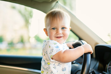Cute little baby boy driving big car, holding steering wheel,smiling and looking forward with interest. Childhood game and dreams