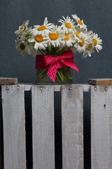 A bouquet of field daisies in a glass vase. On the  wooden box. Genus of perennial flowering plants of the Matricária family (Matricária).