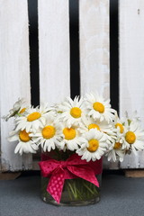 A bouquet of field daisies in a glass vase. Near the wooden box. Genus of perennial flowering plants of the Matricária family (Matricária).