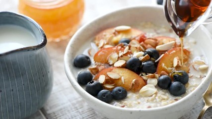 Pouring maple syrup on breakfast porridge with fruits and nuts. Concept of healthy eating, dieting, healthy lifestyle - Powered by Adobe