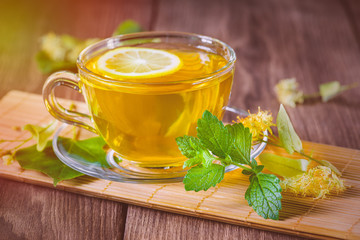 Green tea for health. Cup with fragrant lime tea. Standing wooden table, in the rays of sunlight.