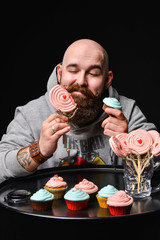 Moscow, Russia, April 2015 - Happy bearded bald man holding two cream cakes on black background.