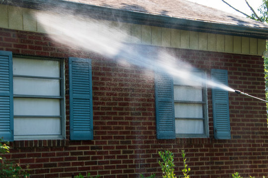 Spray of water on siding and brick work on the side of a building. There are two windows with blue shutters