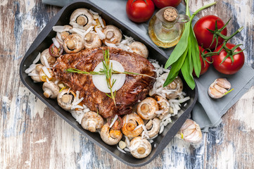Marinated lamb with mushrooms, spices and herbs in a cast-iron mold on a wooden background. Tomatoes and olive oil. Halal meat and food. Top view