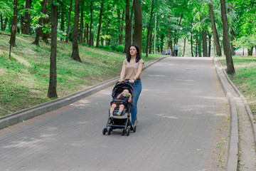 Fototapeta na wymiar Beautiful woman with a child in a pram walks through a summer park.