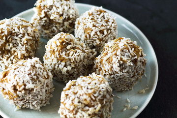 vegetarian raw healthy diet  no bake candies dessert sweets without sugar and gluten-free with coconut, proper nutrition snack on blue plate and black slate background, free copy space for text