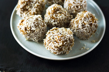 vegetarian raw healthy diet  no bake candies dessert sweets without sugar and gluten-free with coconut, proper nutrition snack on blue plate and black slate background, free copy space for text