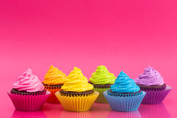 Rainbow Colored Frosted Chocolate Cupcakes on a Bright Pink Background
