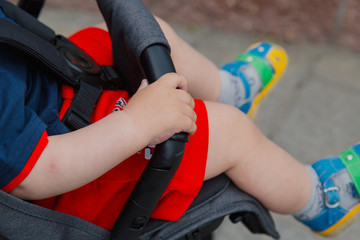 Little boy sitting in a baby carriage on a sunny day.