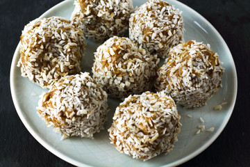 vegetarian raw healthy diet  no bake candies dessert sweets without sugar and gluten-free with coconut, proper nutrition snack on blue plate and black slate background, free copy space for text