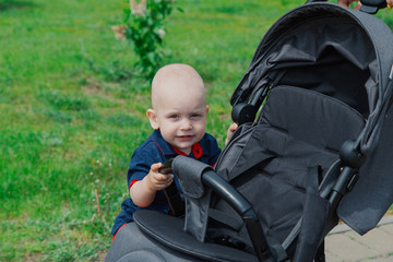 A small child standing by a baby carriage in the warm summer time.