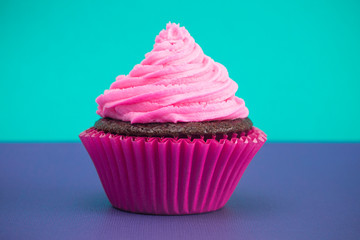 A Single Pink Frosted Chocolate Cupcake on a Purple Surface