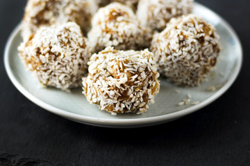 vegetarian raw healthy diet  no bake candies dessert sweets without sugar and gluten-free with coconut, proper nutrition snack on blue plate and black slate background, free copy space for text