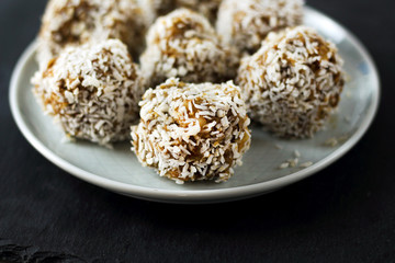 vegetarian raw healthy diet  no bake candies dessert sweets without sugar and gluten-free with coconut, proper nutrition snack on blue plate and black slate background, free copy space for text