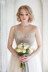 Portrait of an elegant blonde bride in a chic dress with a wedding bouquet in her hands.