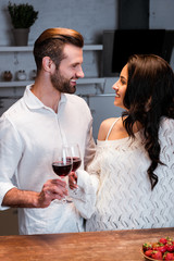 happy couple clinking with wineglasses and looking at each other at wooden table
