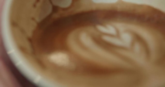 Person raises half full cup of coffee to drink, coffee has a dark rich crema and latte art rosetta