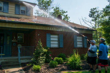 Two young Caucasian men spraying water solution on the front of a house as part of their pressure...