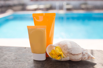 Two jars of sunscreen and shell over the pool with blue water. Skin protection concept.