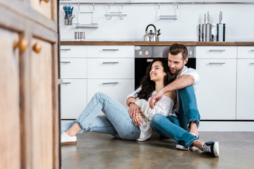 happy couple sitting on floor and hugging at kitchen