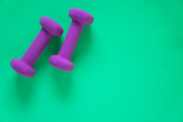 Fitness equipment with womens purple weights/ dumbbells isolated on a teal green background with copyspace