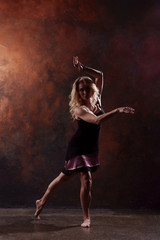 Full-length photo of young dancing blonde in black dress on brown background