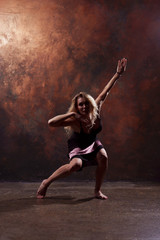 Fototapeta na wymiar Full-length photo of dancing blonde girl looking in camera in short black dress on brown background