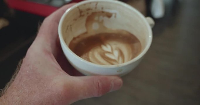 Person lowers half full cup of coffee after drinking, coffee has a dark rich crema and latte art rosetta