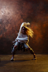 Fototapeta na wymiar Photo of dancing long-haired blonde woman in torn jeans on brown background