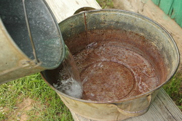 hand wash in the village - clean water flows from the galvanized buckets in the old iron bowl on a wooden bench on a background of green grass