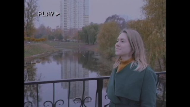 Young woman walks in the autumn park. A girl with blond hair in a green coat walks over the bridge. Old video. Home video archive. Family video. Retro, vintage. Old filmstrip.
