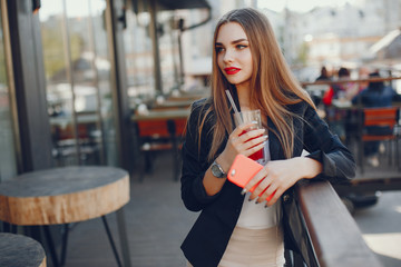 Fototapeta na wymiar Stylish woman in a cafe. Lady with phone. Fashionable girl in a black jacket. Famale drinking a juice