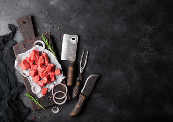 Raw lean diced casserole beef pork steak with vintage meat hatchet and fork with knife on stone background. Rosemary with red onion.Space for text