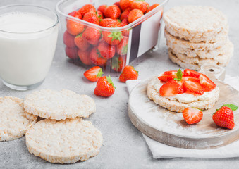 Healthy organic rice cakes with ricotta and fresh strawberries and glass of milk on light stone kitchen background. Top view. Plastic tray of strawberries