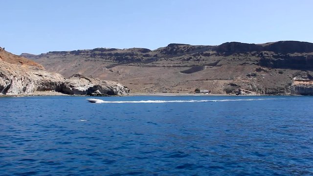 Speed boat sailing by arid coast in Gran Canaria, Spain. Rocky cliffs by the sea in Canary Islands as motorboat passes by. Summer vacation, travel attraction concepts