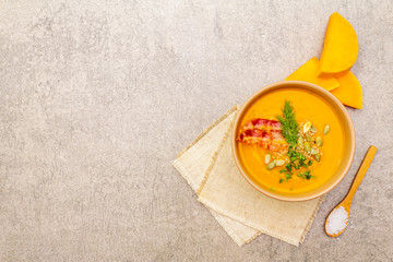 Homemade autumn hot pumpkin cream soup with smocked bacon and seeds. Raw pumpkin, fresh chives, dill, salt in spoon, vintage linen cloth on stone background, top view, copy space.