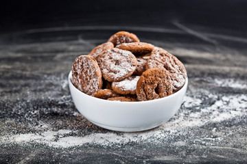 Fresh baked chocolate chip and oat fresh cookies with sugar powder heap in white bowl on black background.