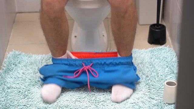 legs of a man sitting on the toilet with blue shorts lowered
