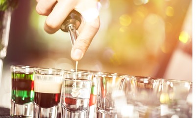 Cropped photo of barman pouring liquor from shaker to set of shot cocktails